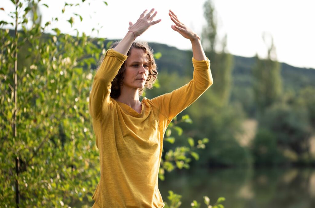 Eva Neumayer-Steiof steht in der Natur, nahe am Wasser und übt Qi Gong